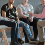 Group of young people sitting in a circle and talking to psychiatrist during a therapy