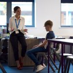 Secondary Or High School Teacher Sitting In Classroom With Unhappy Male Student After Lesson